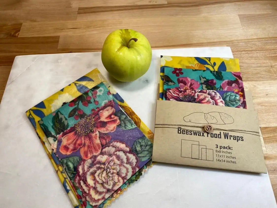3 pack of eco-friendly beeswax food wraps with floral patterns and packaging, next to a green apple.